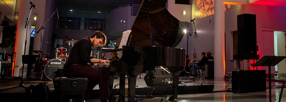 Student playing a grand piano in the Center for the Arts atrium.