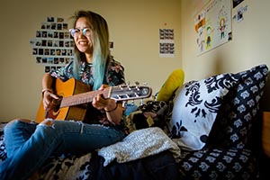 Student playing the guitar in her residence hall room.