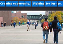 Students walking on campus with a sign overhead that reads: Creating opportunity. Fighting for justice.