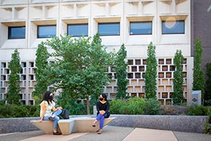 Two students sitting outside in front of a building.
